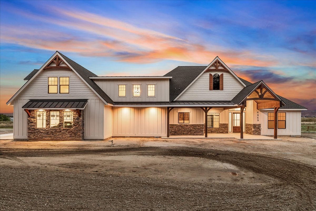Custom farmhouse-style home lit at dusk on a freshly graded lot