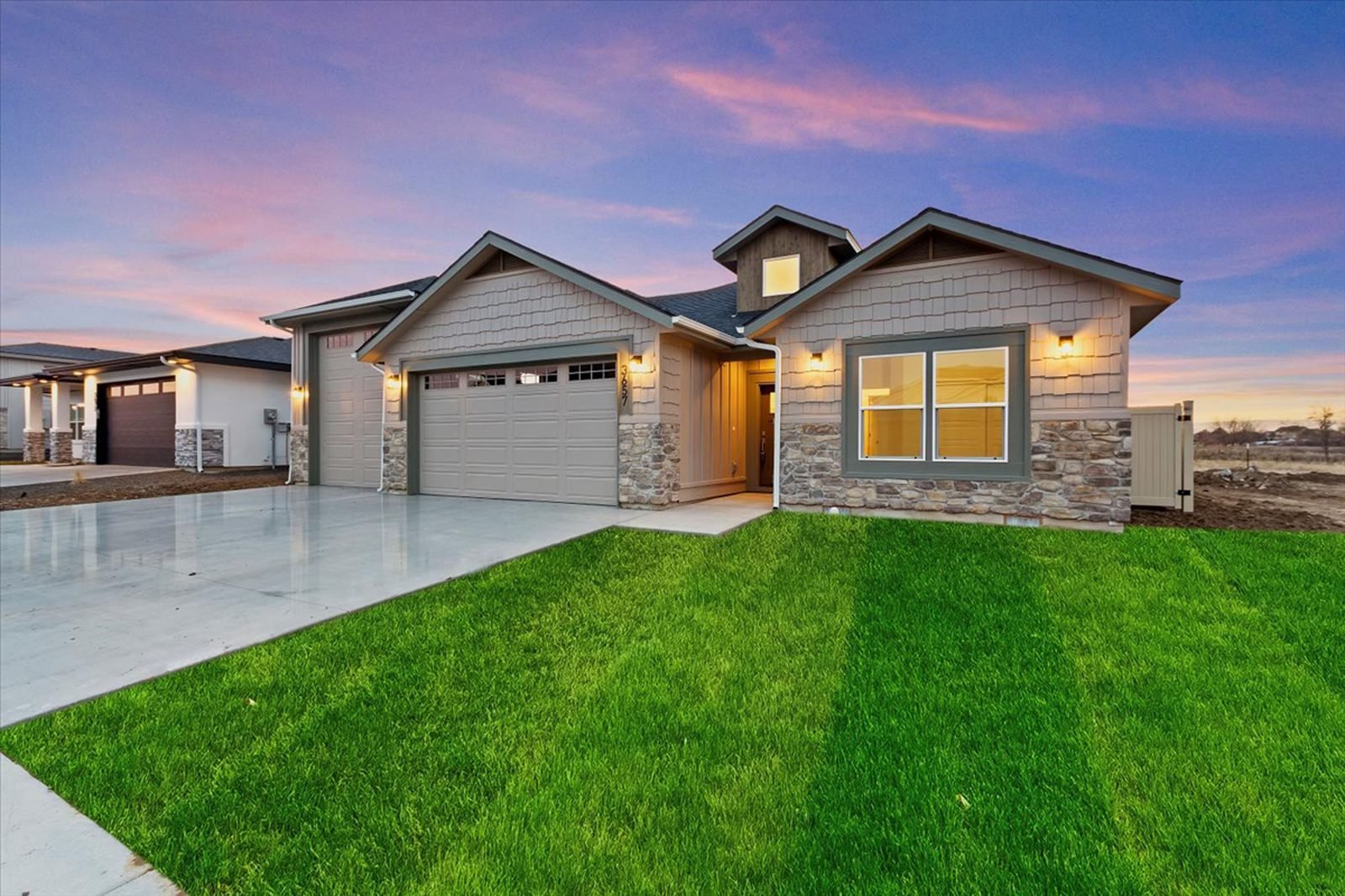 Custom home at dusk with a green lawn and stone accents