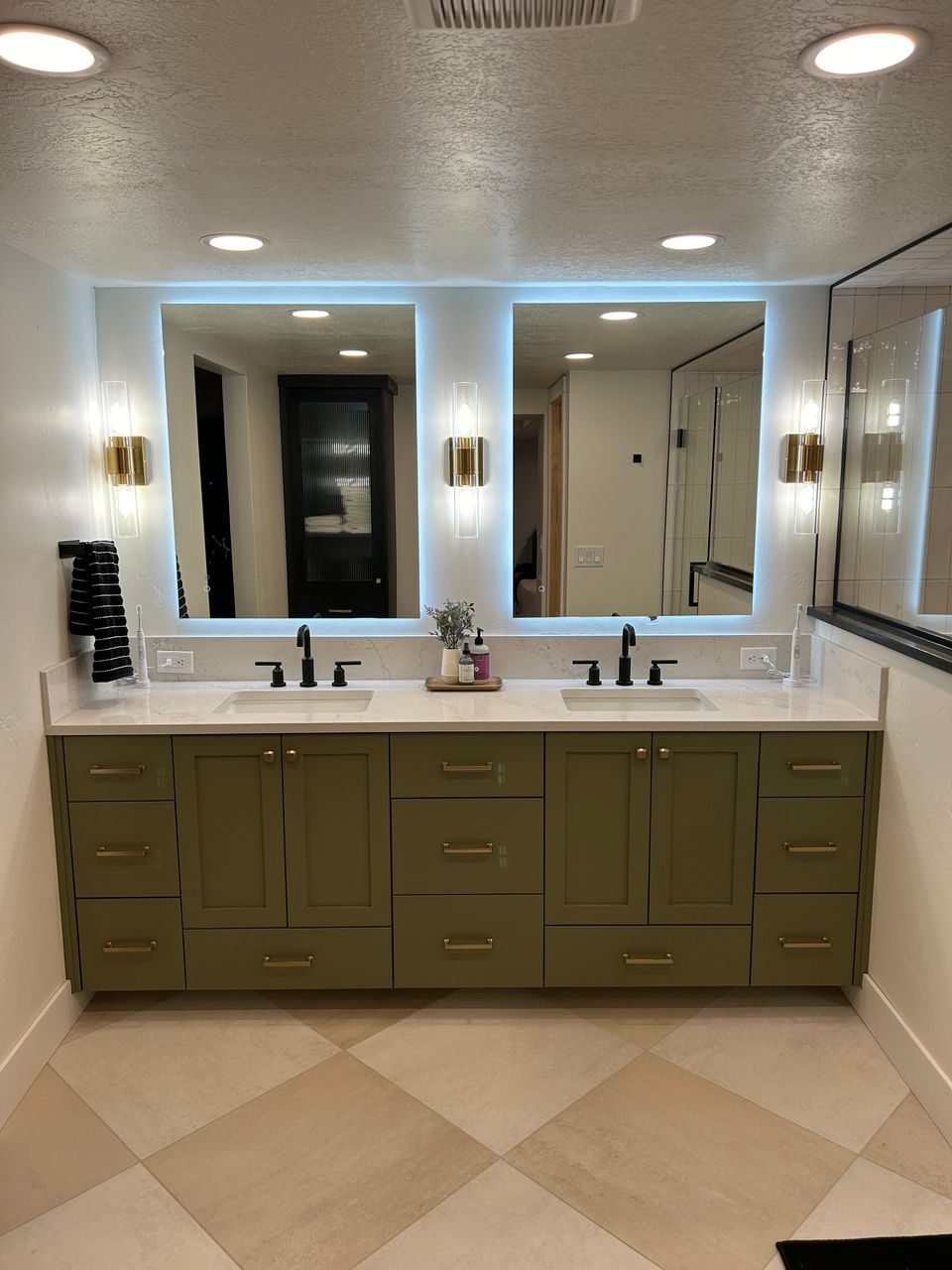 Double vanity with lit mirrors and olive green cabinetry